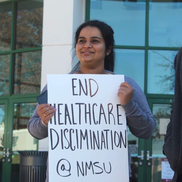 Grad worker with sign reading End Healthcare Discrimination @ NMSU