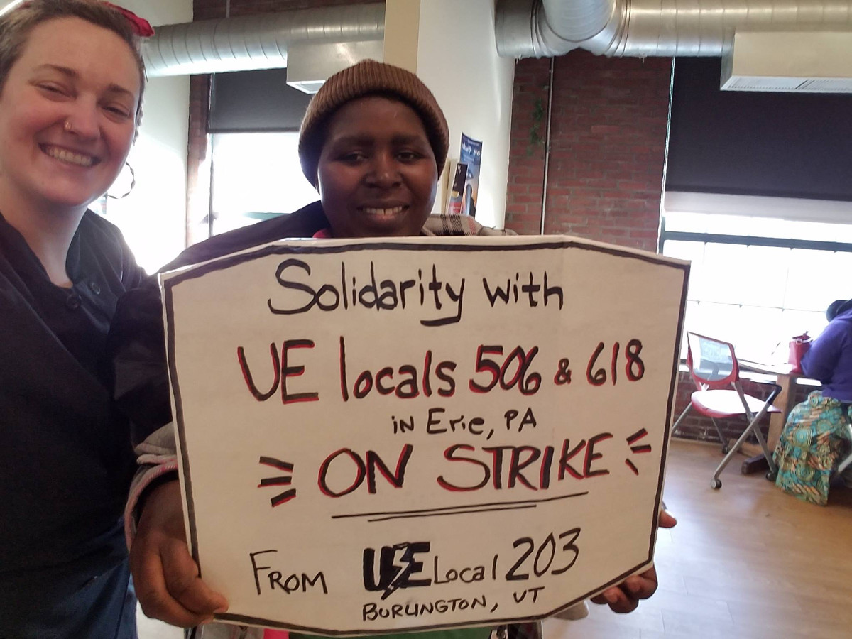 Two UE members with a sign reading "solidarity with UE Locals 506 & 618 in Erie, PA on strike from UE Local 203 Burlington, VT"