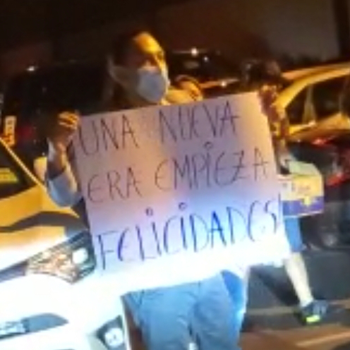 Woman holding a sign reading Ua nueva era empieza felicidades (A new era begins congratulations)