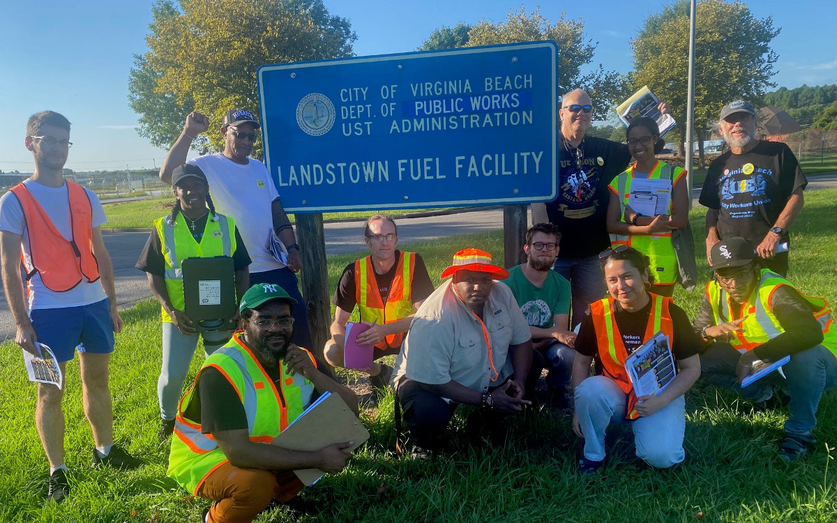 UE members, staff and community allies pose at a City of Virginia Beach Department of Public Works sign