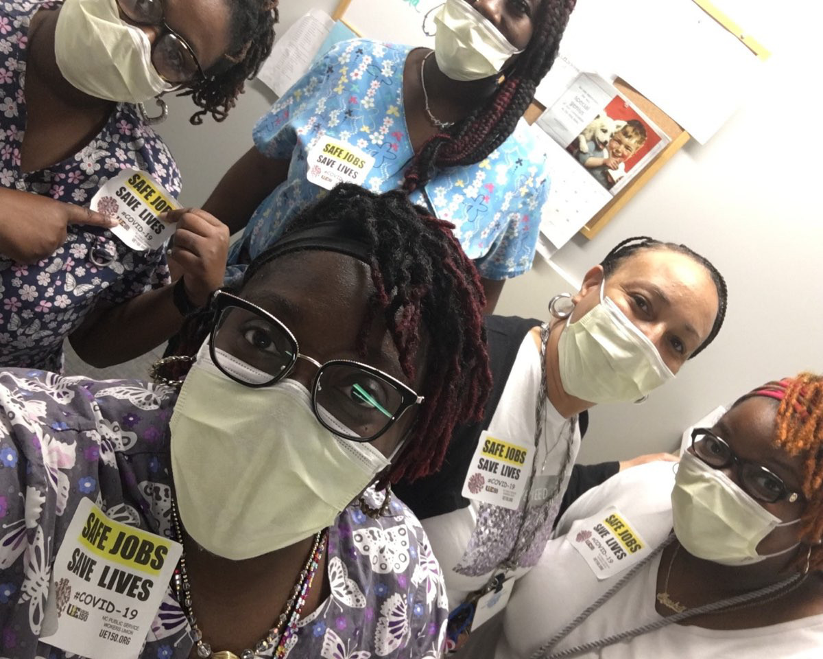A group of black women wearing medical scrubs, masks, and Safe Jobs Save Lives stickers