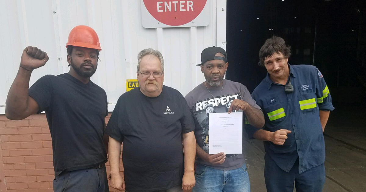 Four workers, one holding up a copy of their contract, one with a raised fist