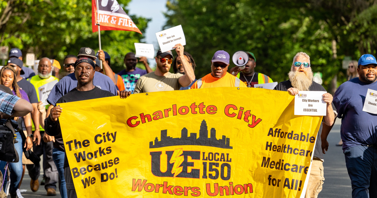 Charlotte city workers marching behind a Charlotte City Workers Union/UE Local 150 banner that reads The City Works Because We Do! and Affordable Healthcare Medicare for All!