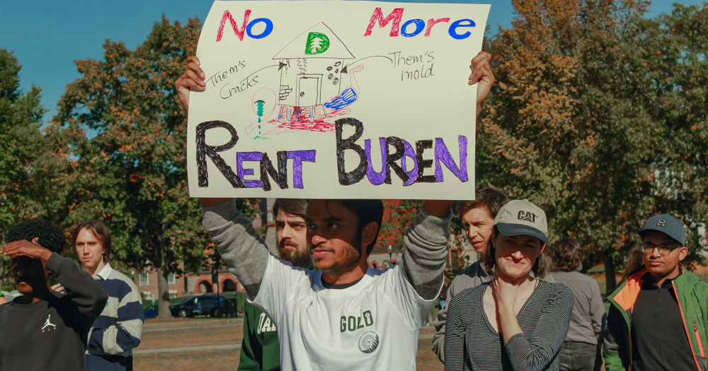 Dartmouth college graduate worker holds a sign reading No More Rent Burden