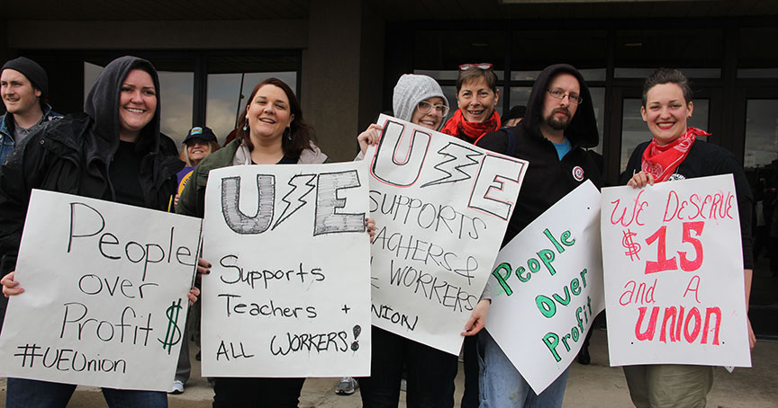 Six UE Young Activists holding signs saying "People Over Profit," "UE Supports Teachers & All Workers" and "We Deserve $15 and a Union"
