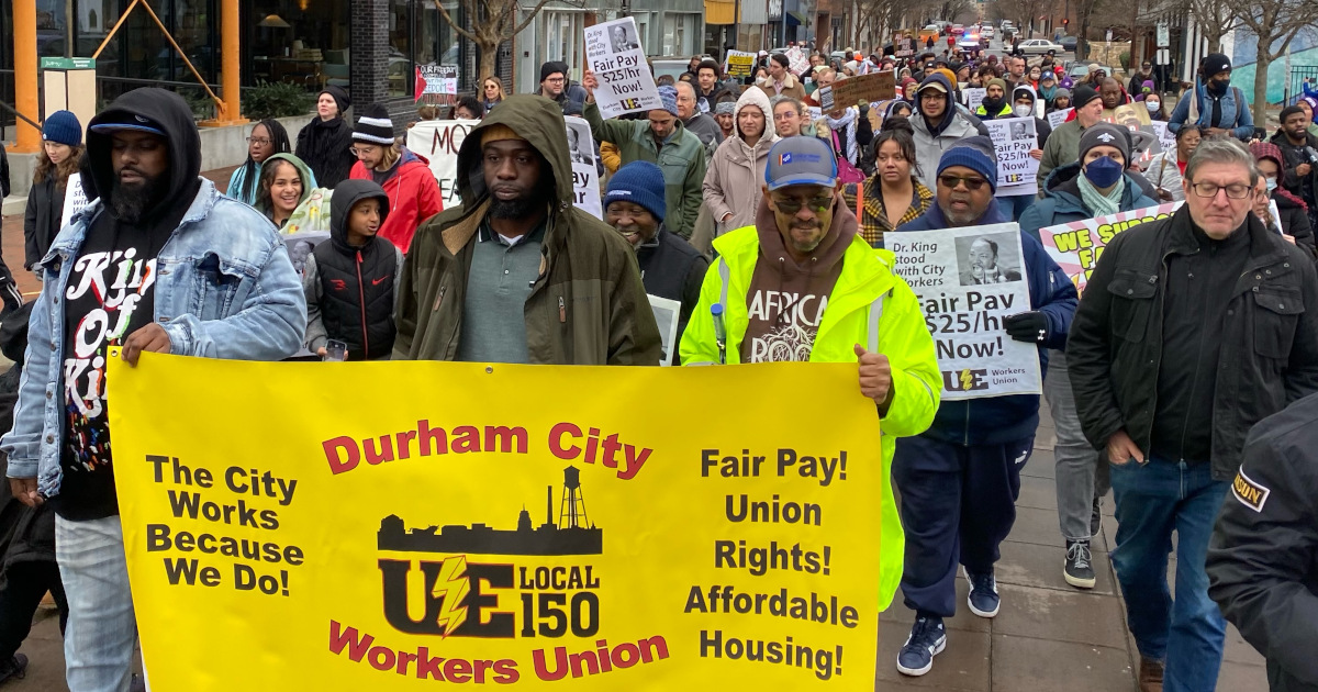 A group of workers marching with a Durham City Workers Union UE Local 150 banner