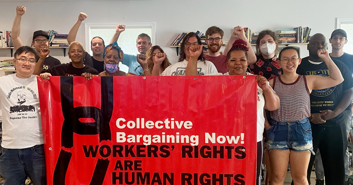 Workers with raised fists behind a banner reading Collective Bargaining Now! Workers Rights Are Human Rights