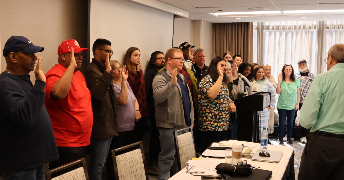 Approximately twenty UE members with their right hands raised, being sworn in to the offices they have just been elected to