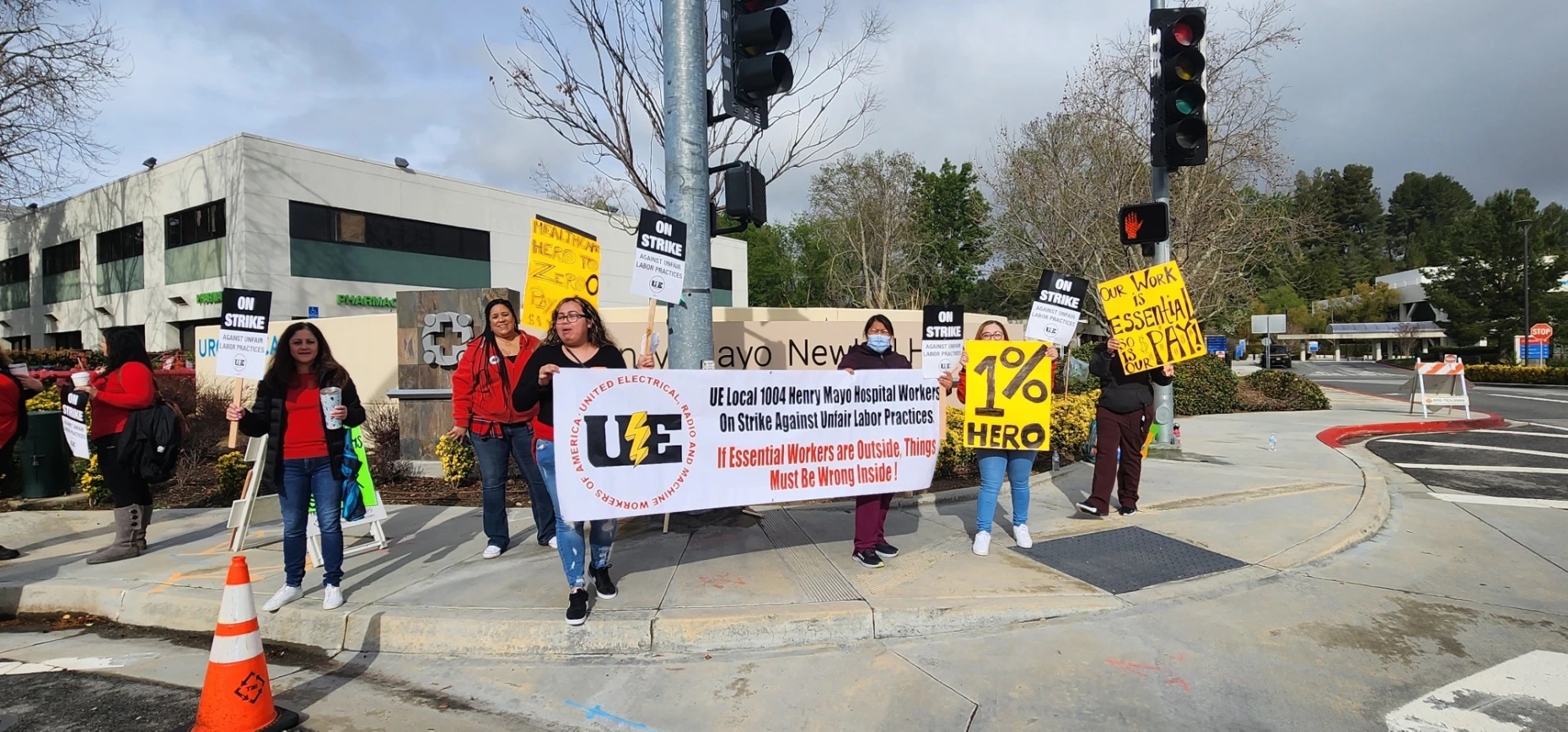 Striking workers with a banner reading UE Local 1004 Henry Mayo Hospital Workers On Strike Against Unfair Labor Practices. If Essential Workers Are Outside, Things Must Be Wrong Inside!