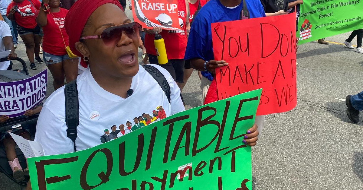 Woman carrying a sign reading Equitable Employment for All Workers