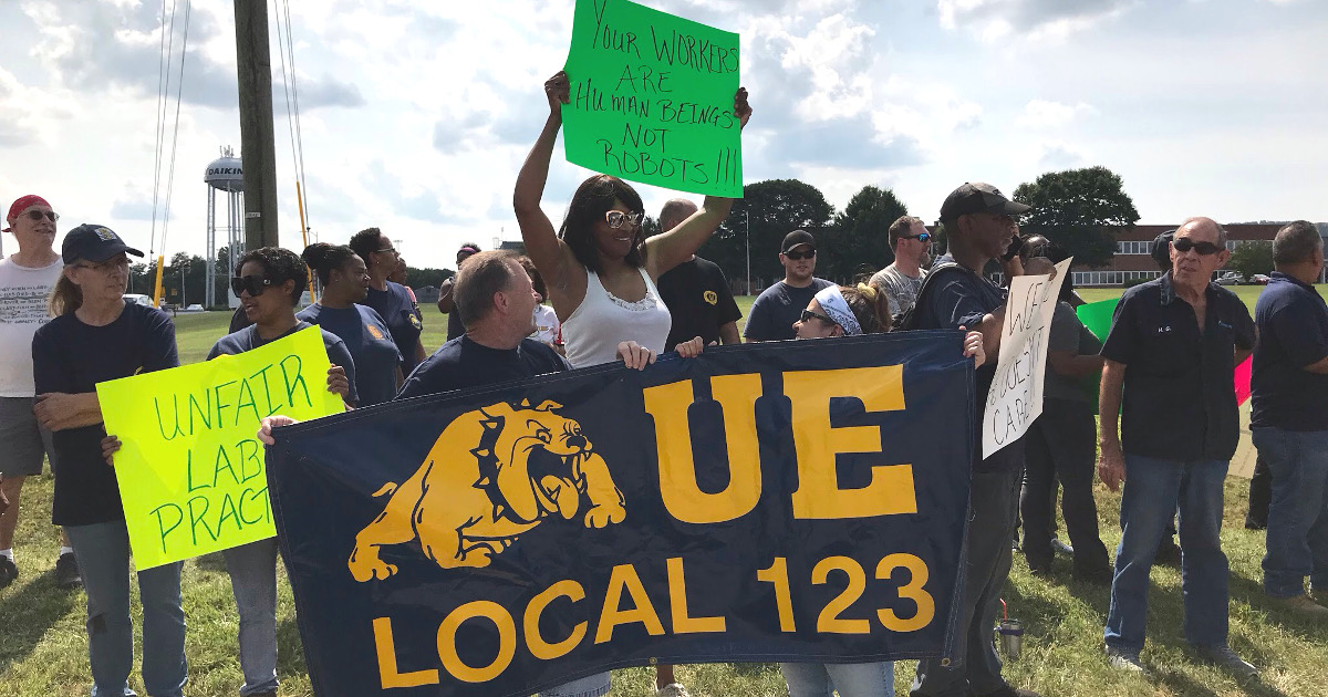 Local 123 members rally in front of the plant with a sign that says Your Workers Are Human Beings Not Robots