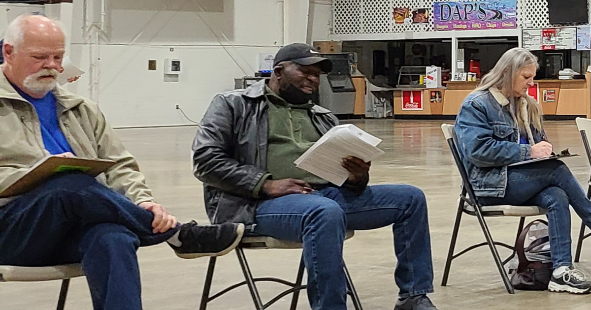 Two men and a woman sitting in folding chairs reading contract summaries