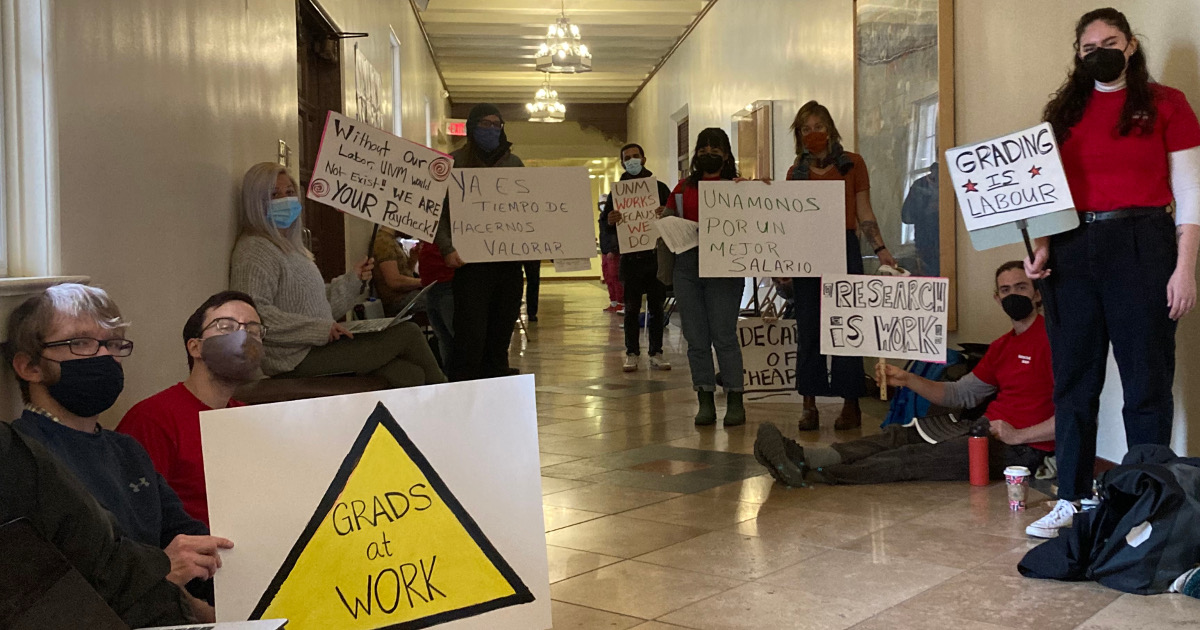 Graduate workers in hallway of university building with signs reading Grads At Work, Research Is Work, and Grading Is Labour