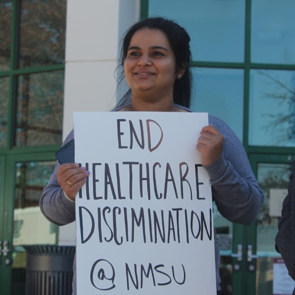 Graduate worker with sign reading End healthcare discrimination at NMSU