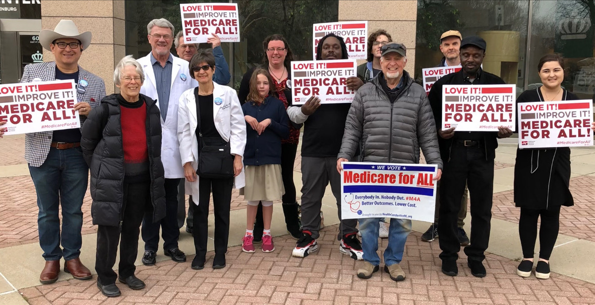 Racially diverse group of men and women with Love It! Improve It! Medicare for All! signs