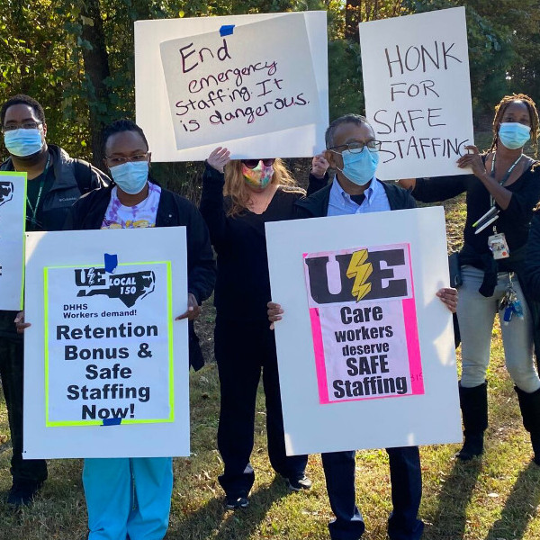 Masked workers holding signs demanding safe staffing and hazard pay