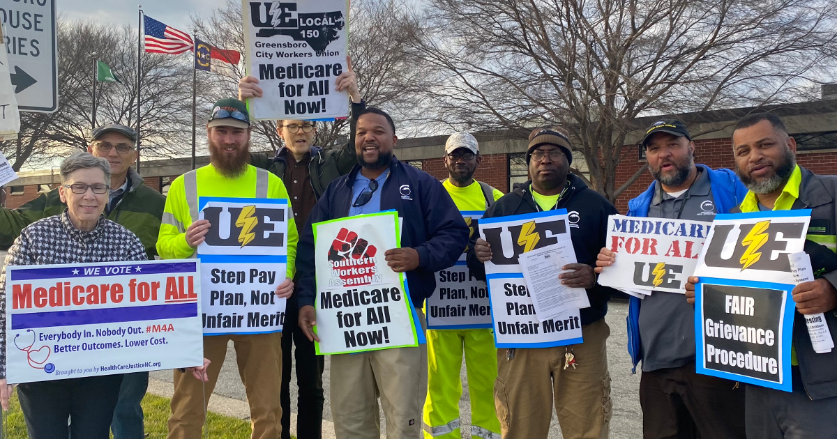 Group of white and Black people holding signs reading "Step Pay Plan, Not Unfair Merit," "Fair Grievance Procedure," and "Medicare for All"