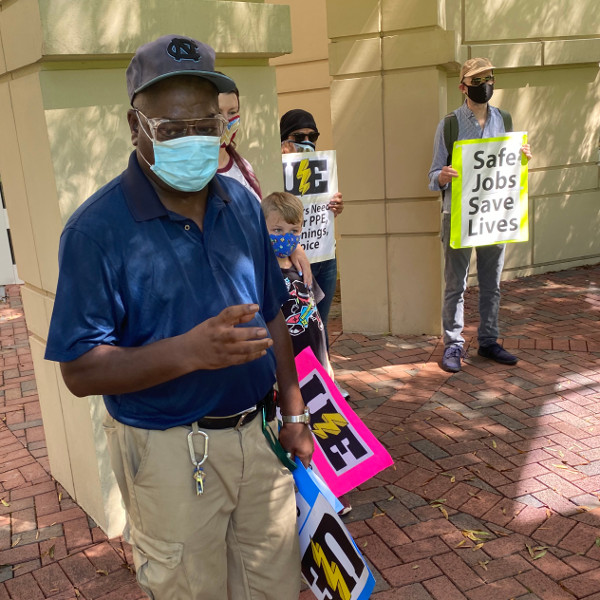 Worker in mask speaking while other hold UE and Safe Jobs Save Lives signs