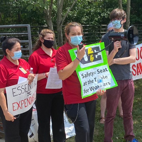 A group of women workers, one of them speaking into a megaphone which is held by a young man