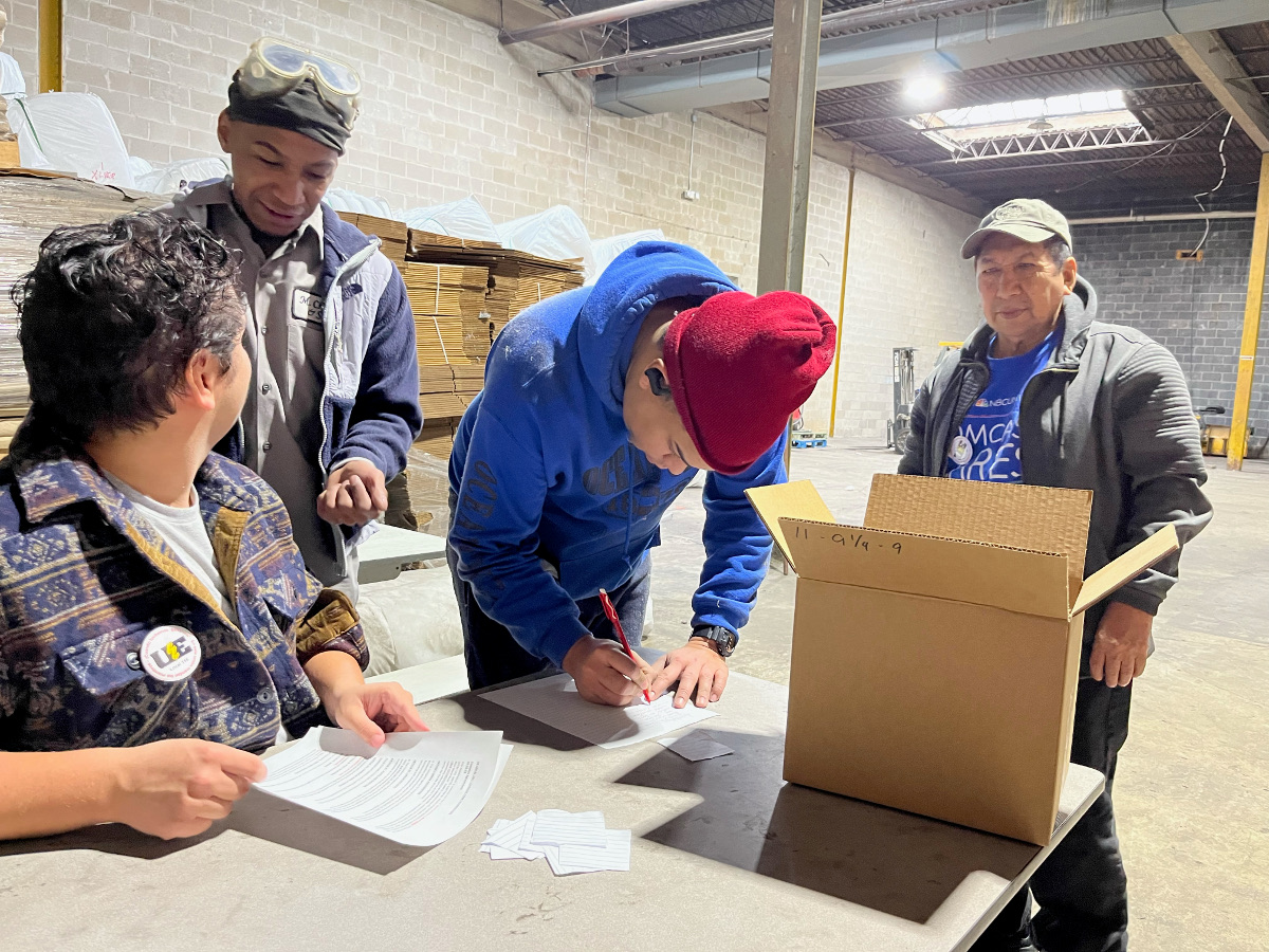 A worker talks to a man seated at a table while other workers vote