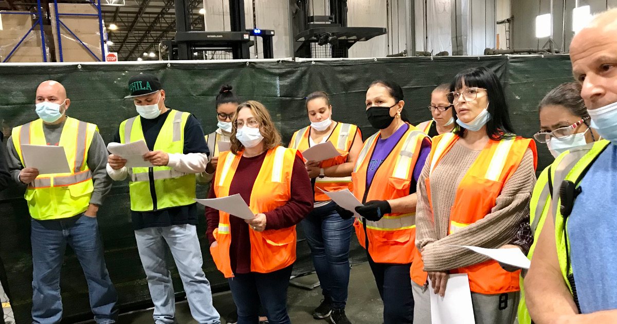 A group of workers standing in a warehouse looking at copies of the tentative agreement