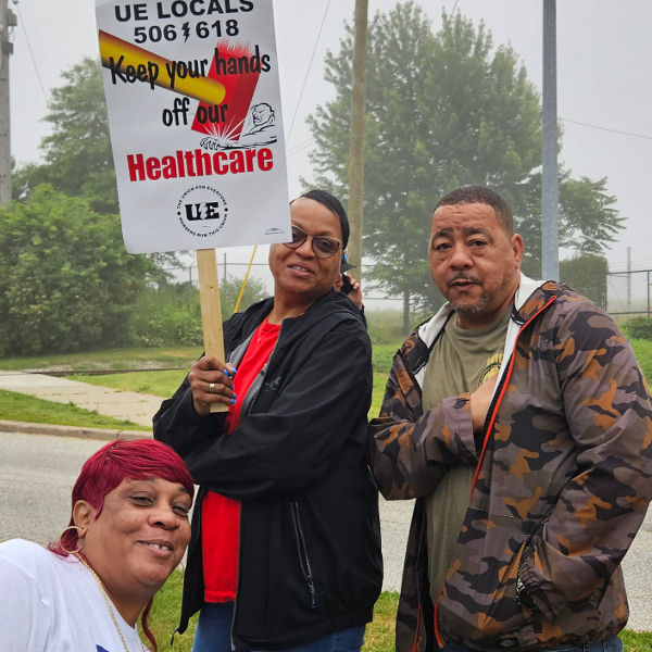 Three UE Local 506 strikers with picket sign reading Keep your hands off our healthcare