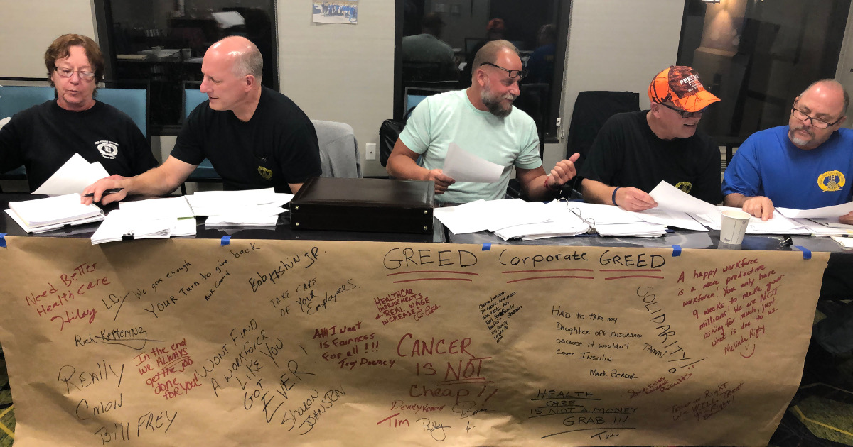 Local 625 committee members sitting behind a table with butcher paper filled with messages to the company