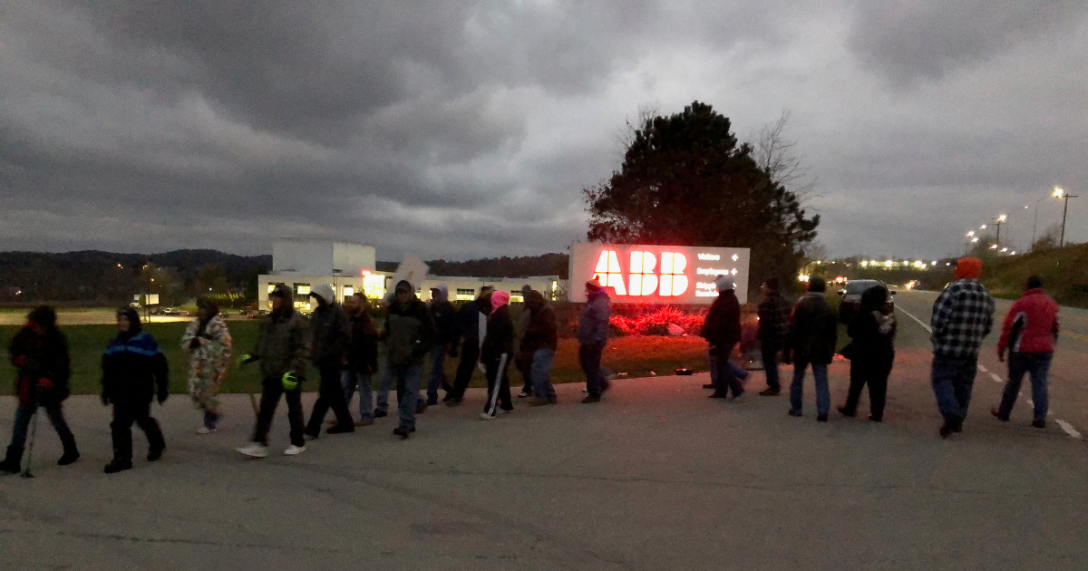 UE members picketing at dawn in front of a neon-lit "ABB" sign