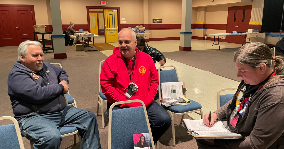 Three UE members sitting on chairs, talking to each other, with Summer Lee literature