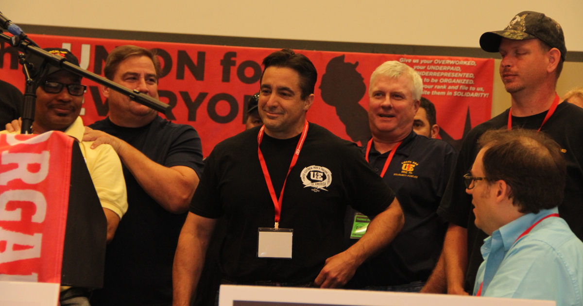 A group of six men on stage, most wearing UE gear