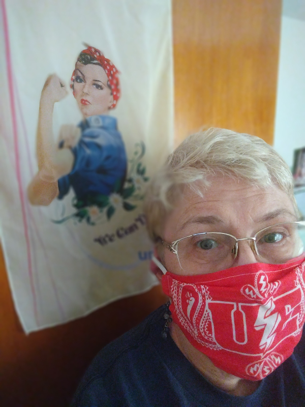 Woman in a UE mask in front of an image of Westinghouse Wendy (a woman in a kerchief rolling up her sleeves in a Rosie-the-Riveter pose)