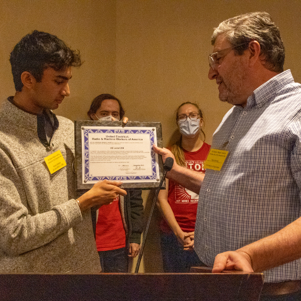 UE Director of Organization Mark Meinster presents a charter for UE Local 256 (MIT GSU) to Nishad Gothaskar