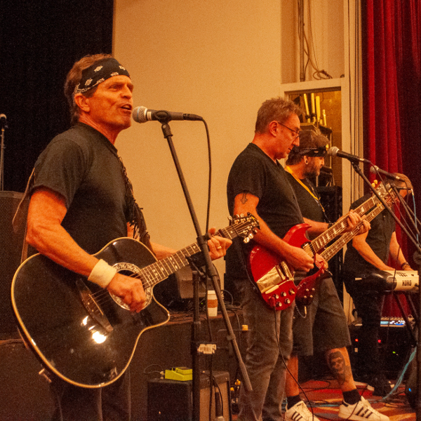 Man singing and playing guitar accompanied by a guitarist, bass player, and keyboard player.