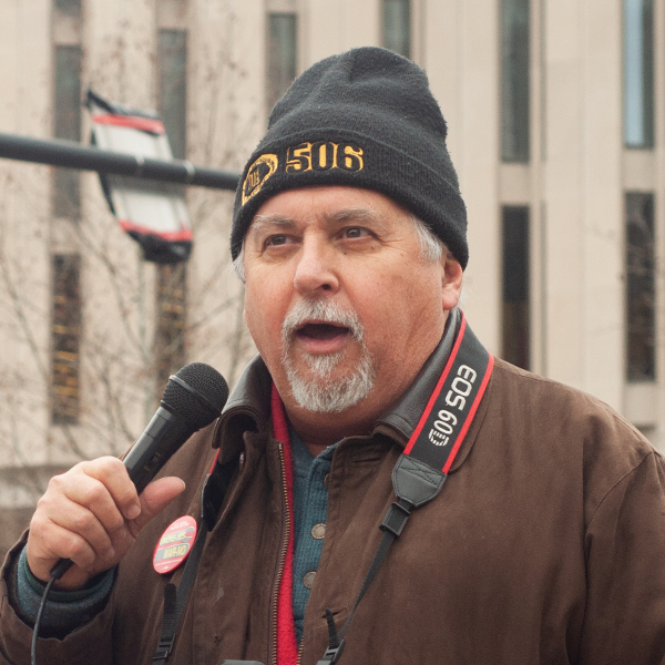 Man wearing a UE Local 506 hat speaking into a microphone