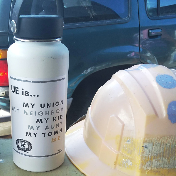 Photo of water bottle with sticker reading "UE is... my union, my neighbor, my kid, my aunt, my town, me." and a UE Local 506 logo. Next to the water bottle is a hard hat.