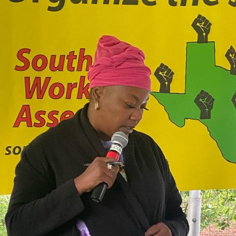 A woman speaking into a microphone in front of a Southern Workers Assembly banner